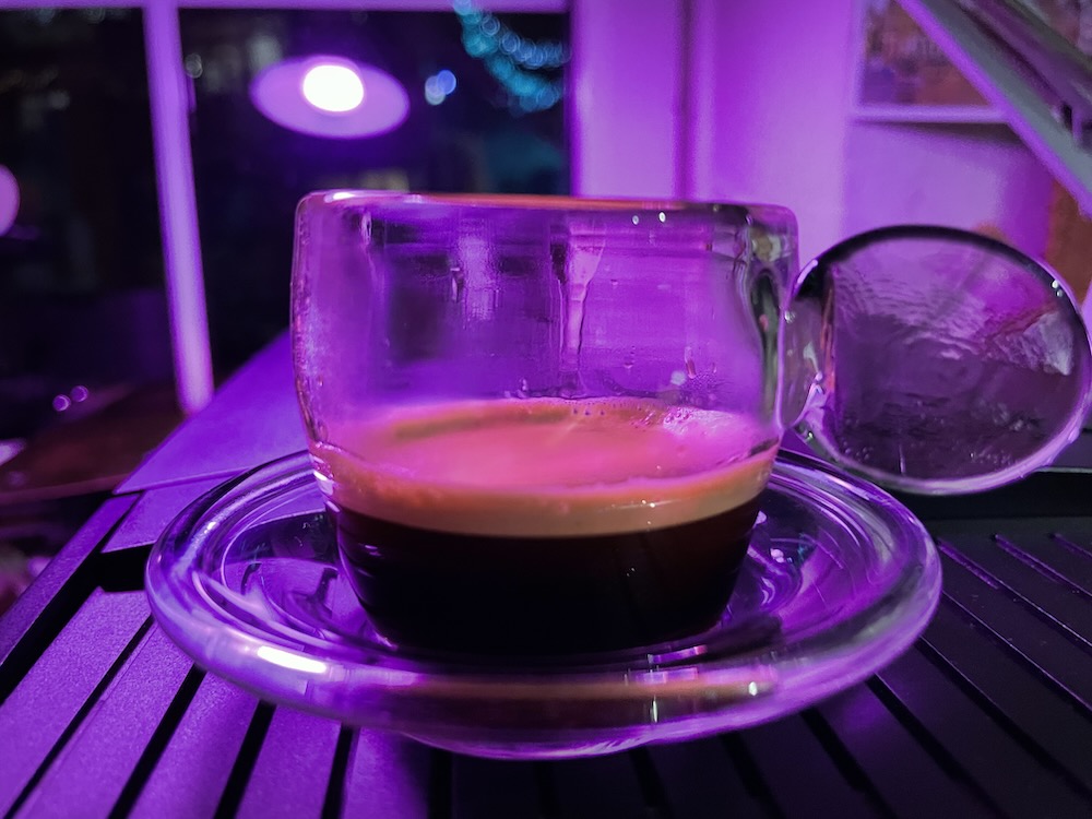 espresso freshly brewn in a glass cup illuminated with low violet light.